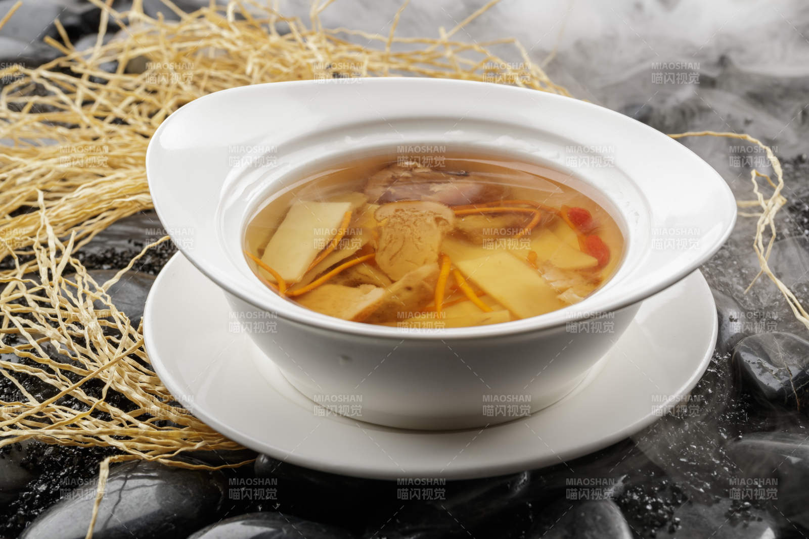 白色汤盆装的至尊菌皇汤摆放在黑色鹅卵石上图片