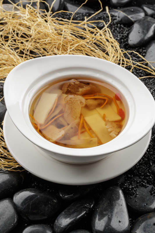 白色汤盆装的至尊菌皇汤摆放在黑色鹅卵石上图片