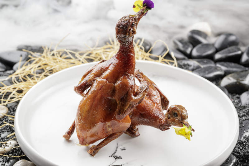 白色圆盘装的生炸乳鸽摆放在黑色鹅卵石上图片