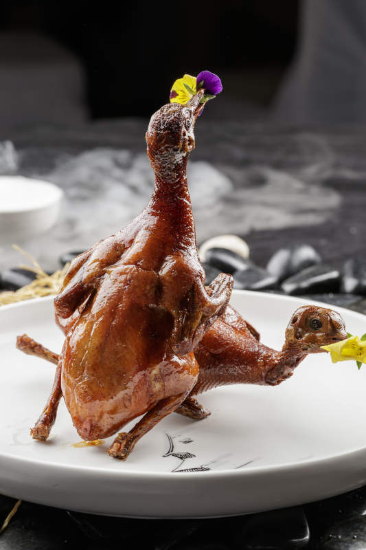 白色圆盘装的生炸乳鸽摆放在黑色鹅卵石上图片