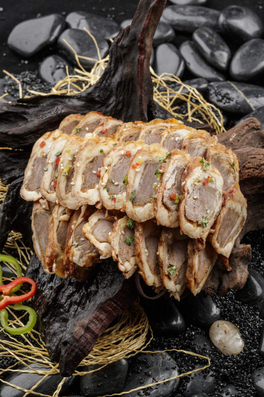 崖柏根装的蒙古烤羊里脊摆放在黑色鹅卵石上图片