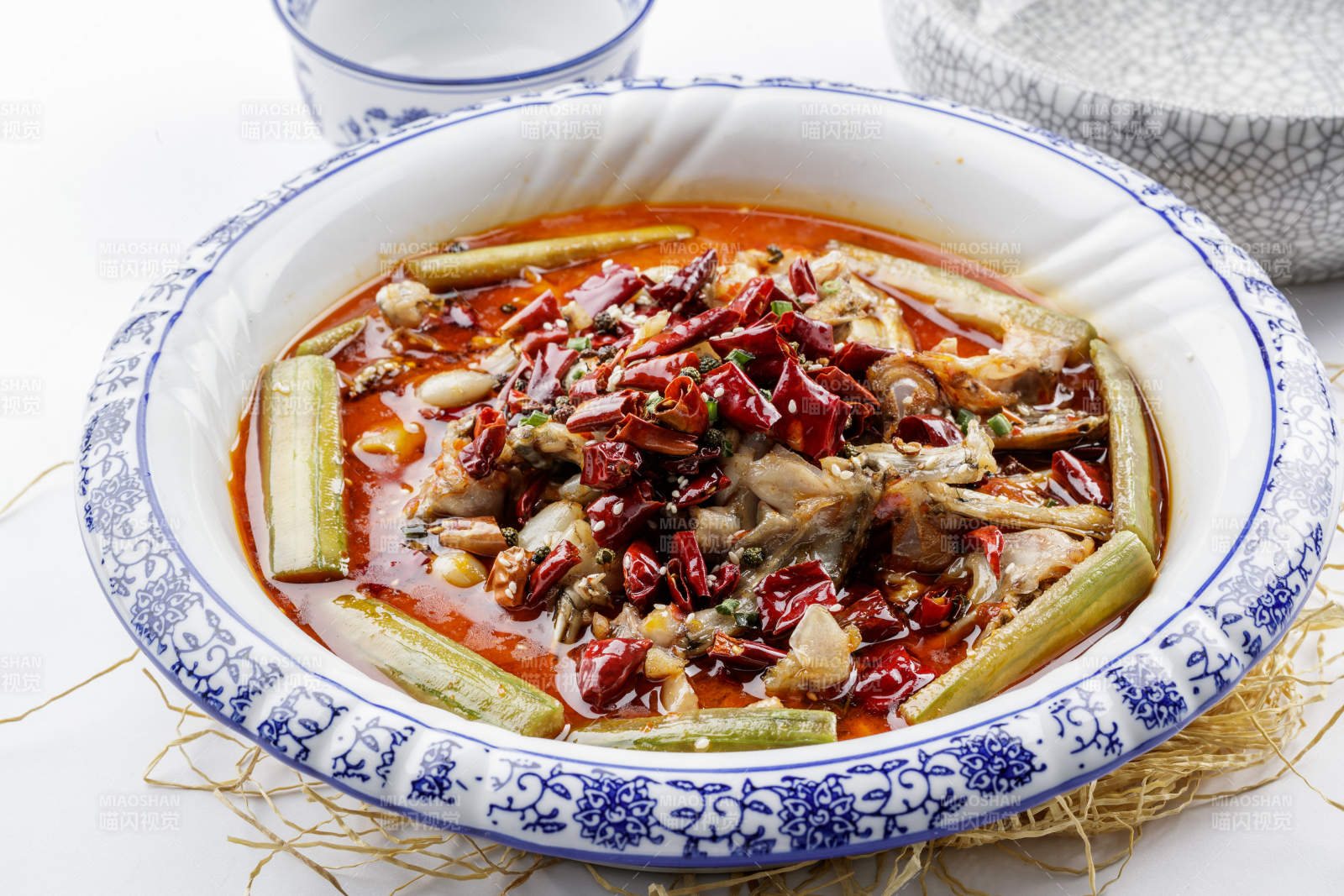 青花瓷盘装的湘味馋嘴蛙摆放在白色底板上图片