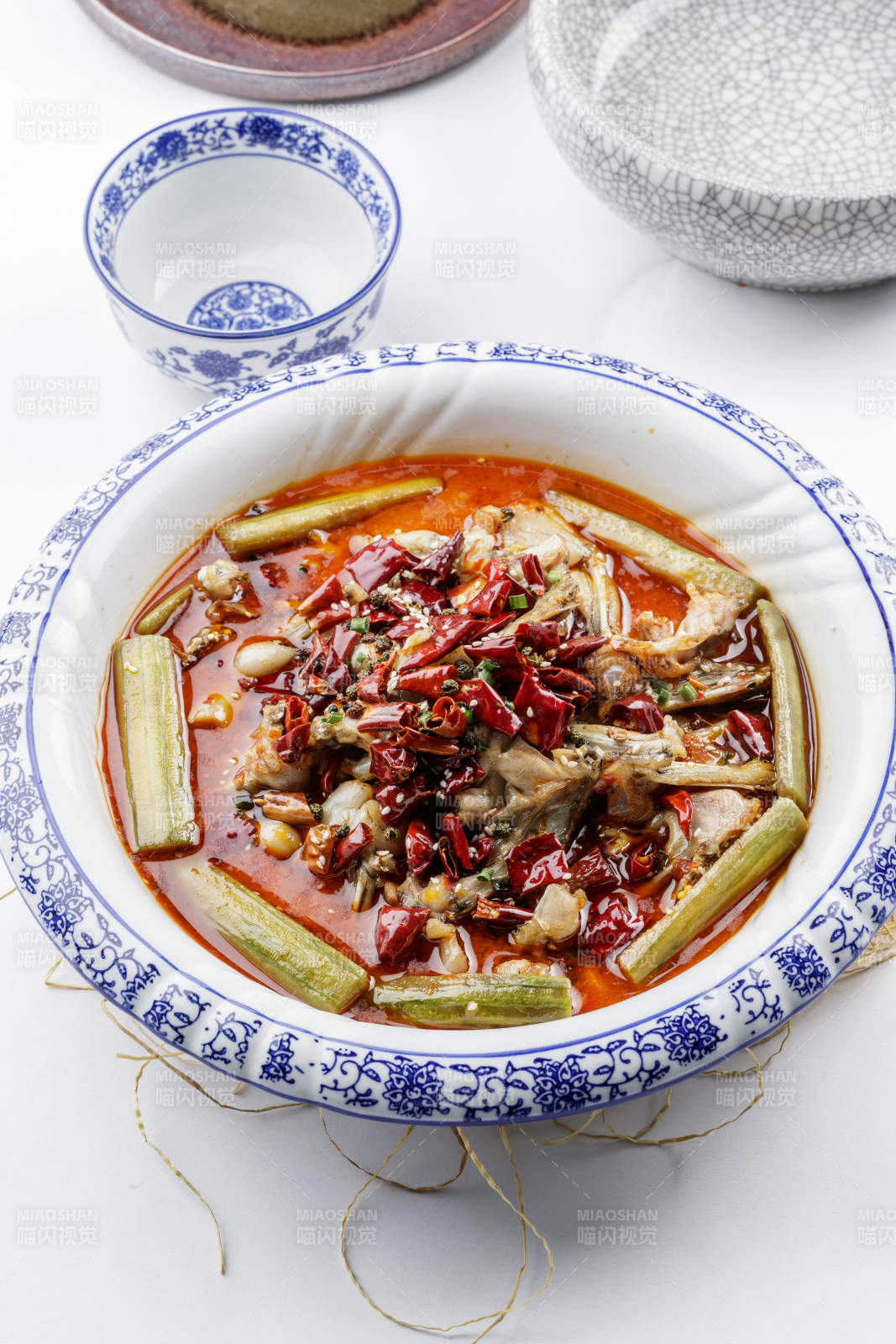 青花瓷盘装的湘味馋嘴蛙摆放在白色底板上图片