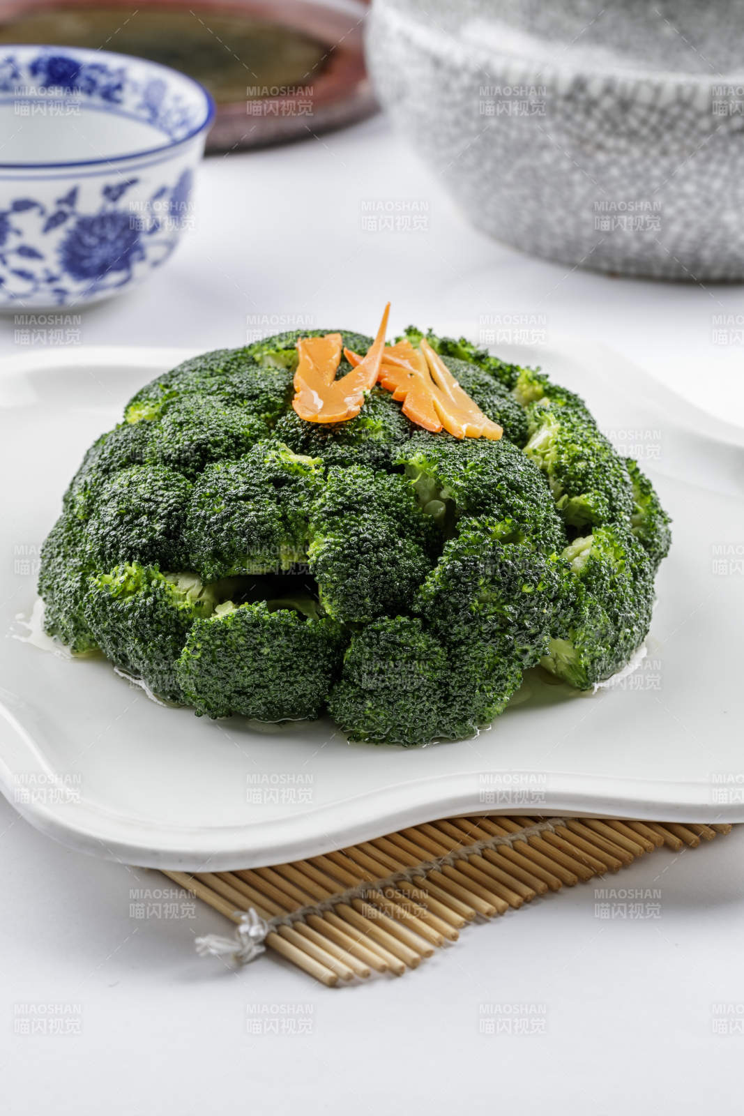 白色梅花瓷盘装的白灼西蓝花摆放在寿司帘上图片