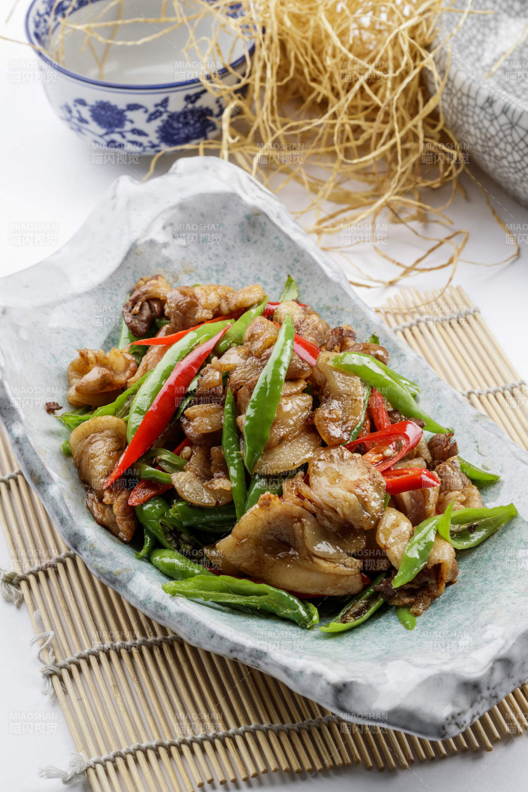 青瓷盘装的湘味小炒肉摆放在寿司帘上图片