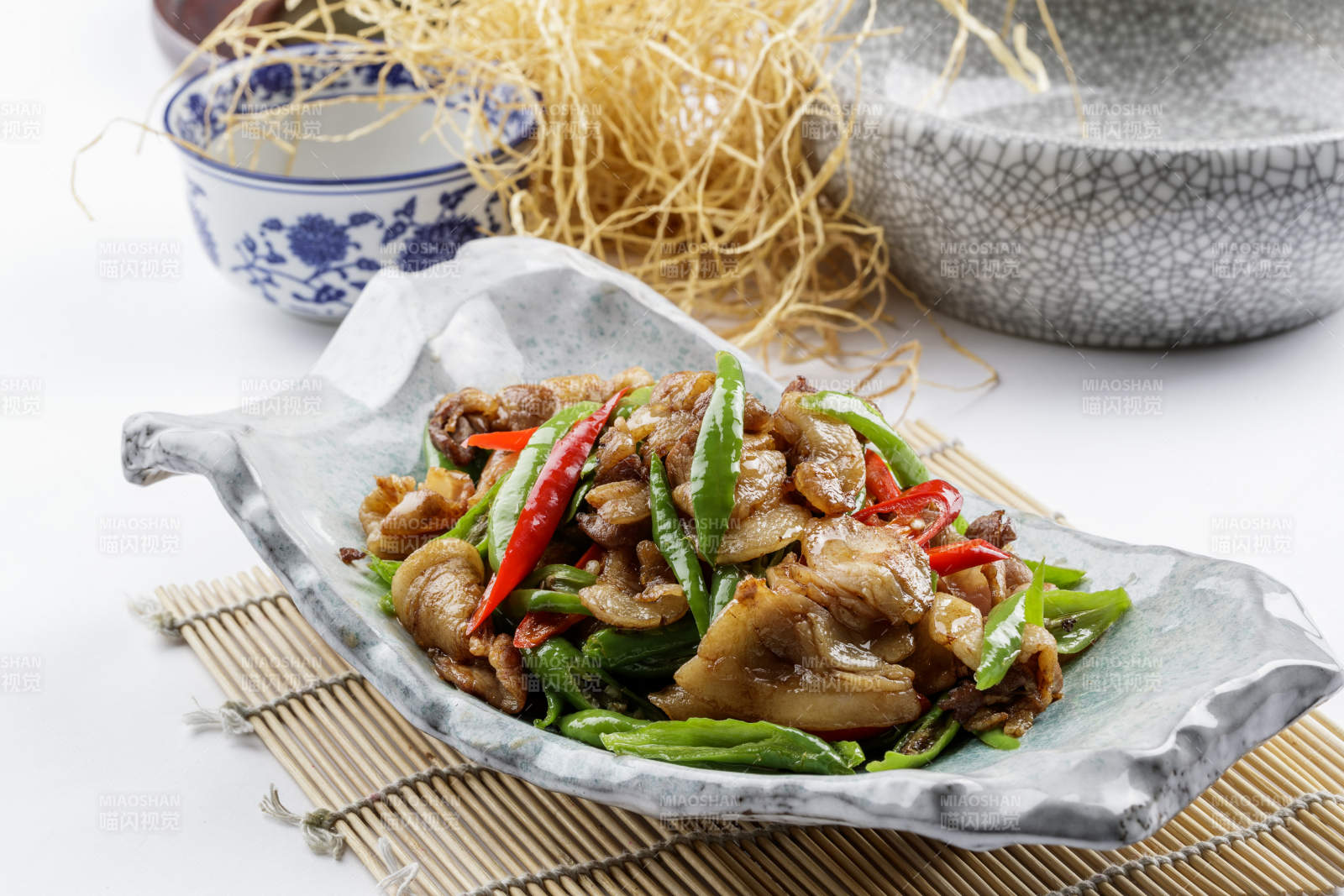 青瓷盘装的湘味小炒肉摆放在寿司帘上图片