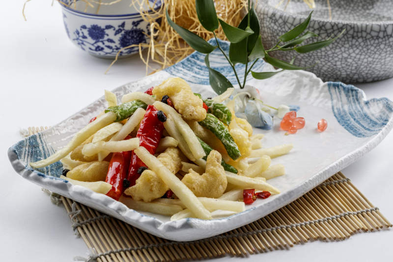 花纹瓷盘装的虎皮双椒薯香蒜香肉摆放在寿司帘上图片