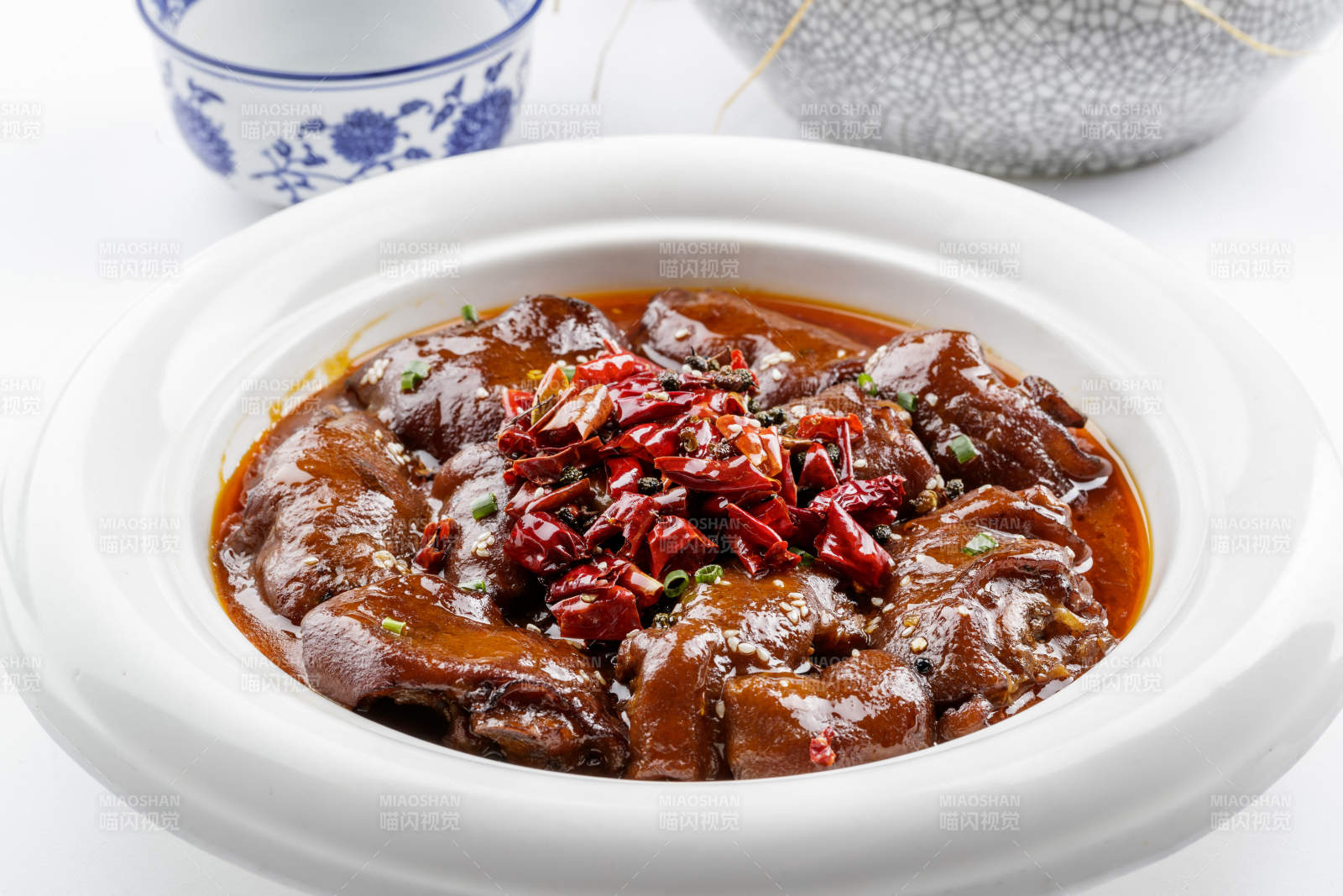 白色圆盘装的香辣猪蹄摆放在白色背景上图片