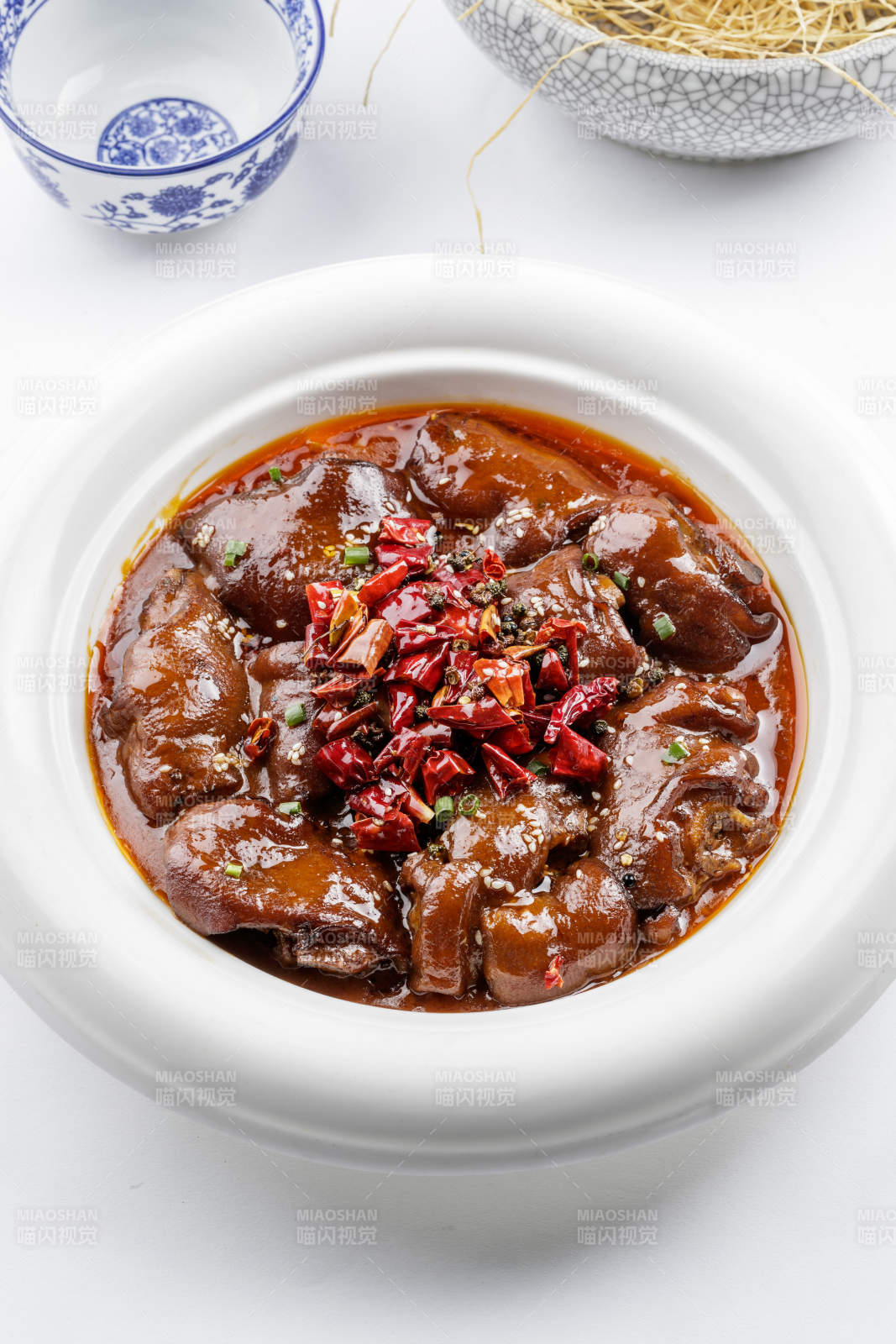 白色圆盘装的香辣猪蹄摆放在白色背景上图片