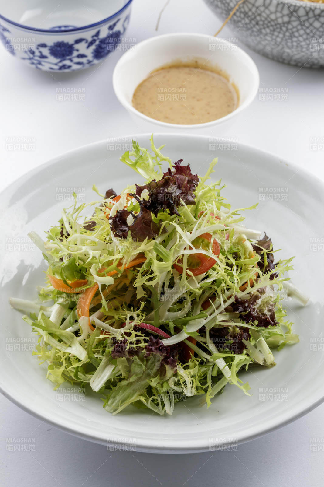 青色瓷盘装的呛拌苦菊摆放在白色背景上图片