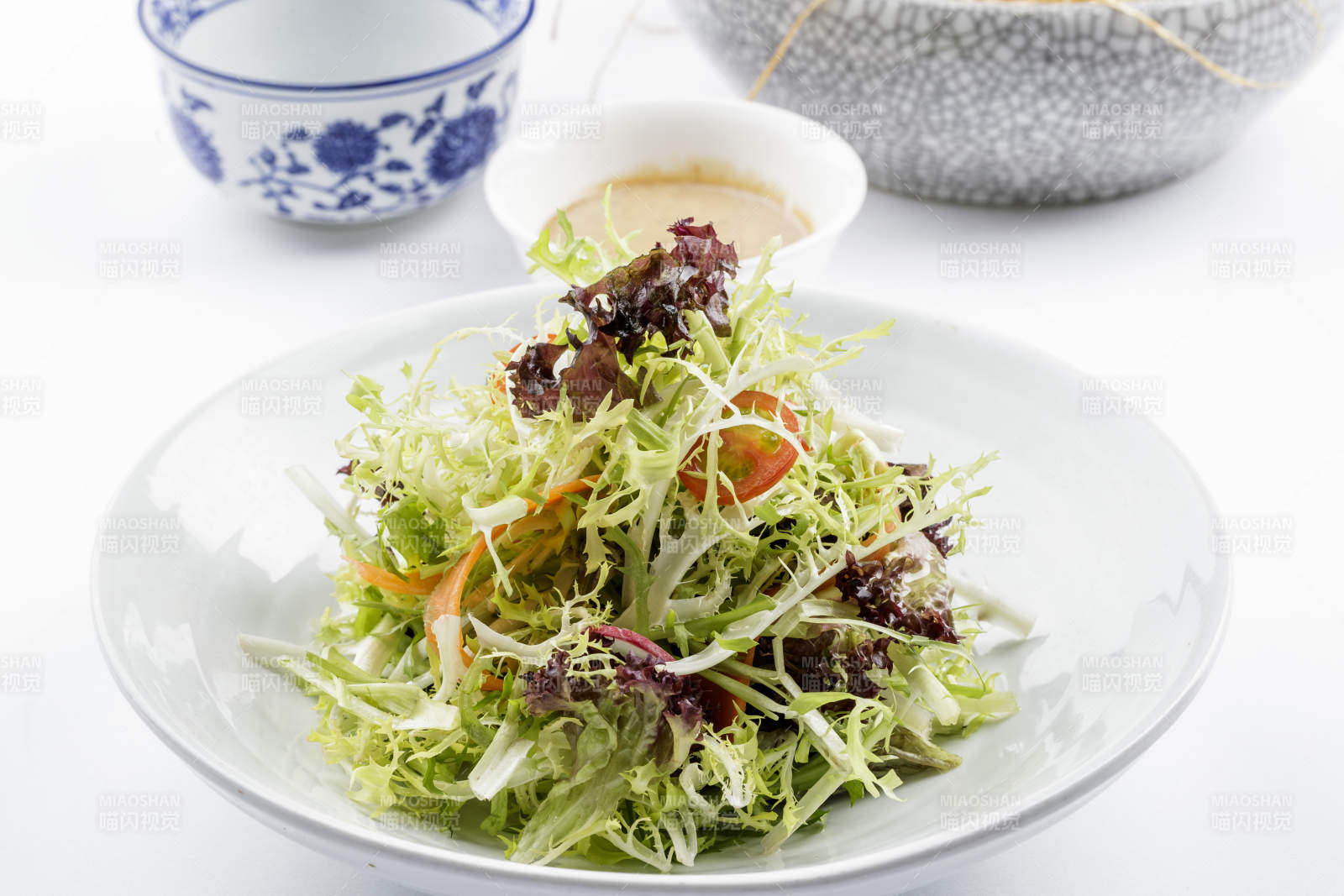 青色瓷盘装的呛拌苦菊摆放在白色背景上图片