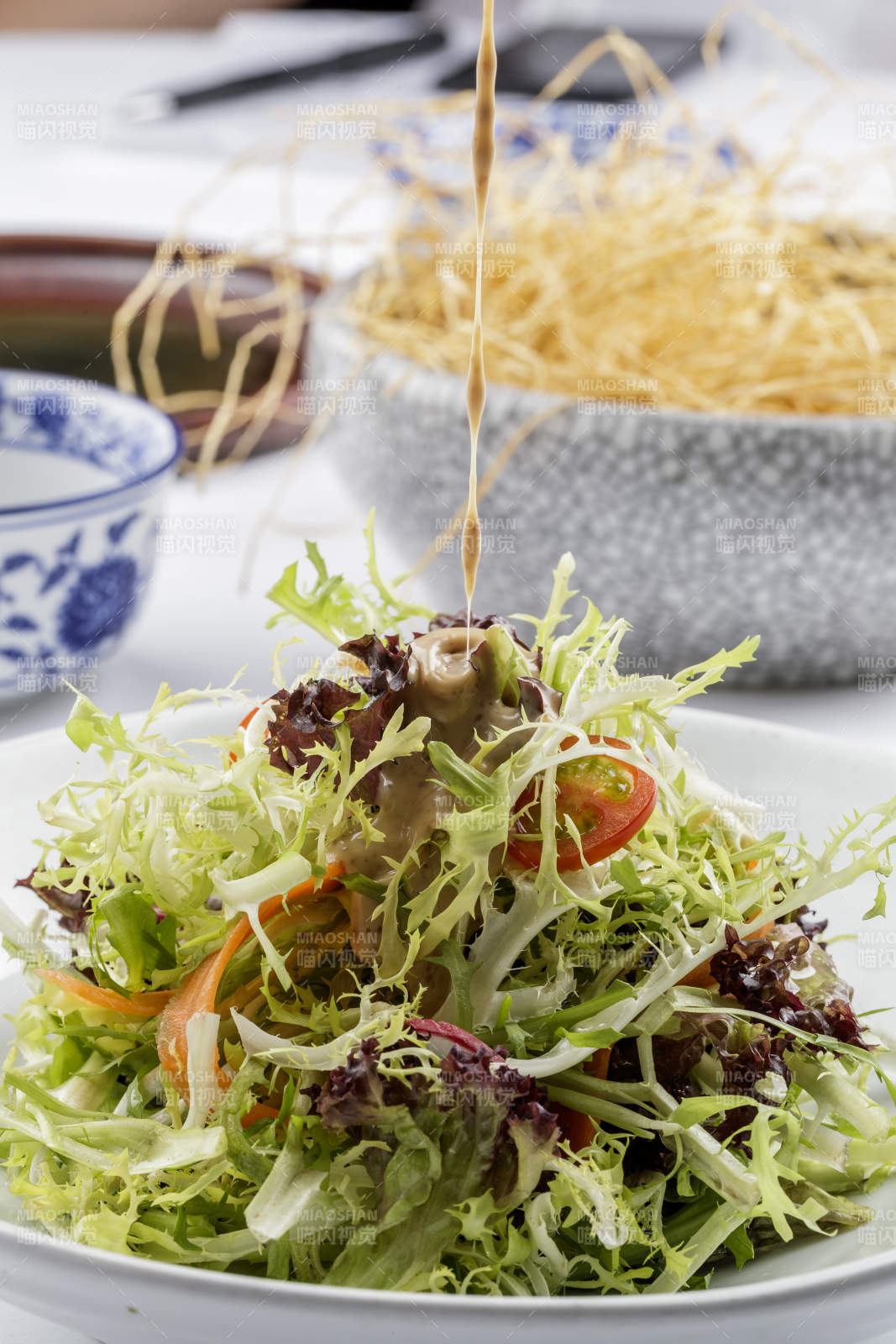 青色瓷盘装的呛拌苦菊摆放在白色背景上图片