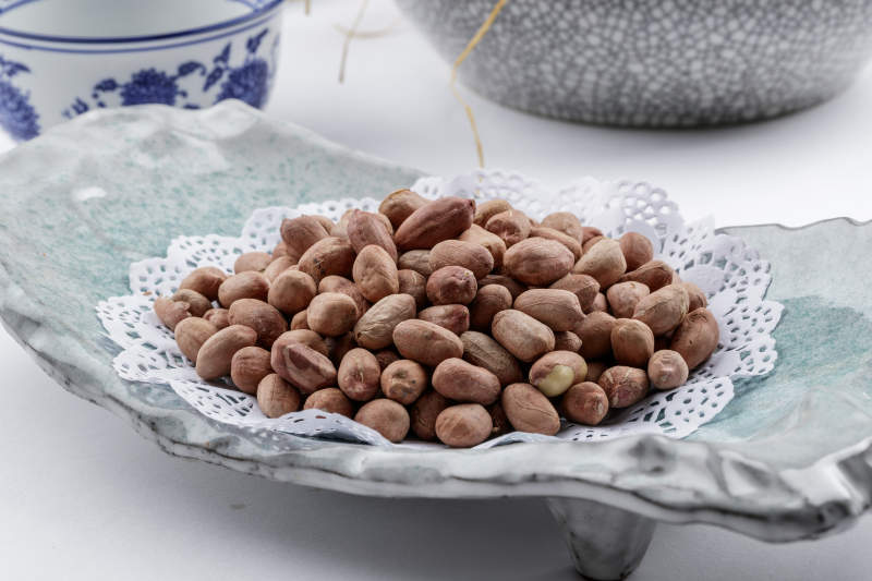 青瓷盘装的有机花生米摆放在白色背景上图片