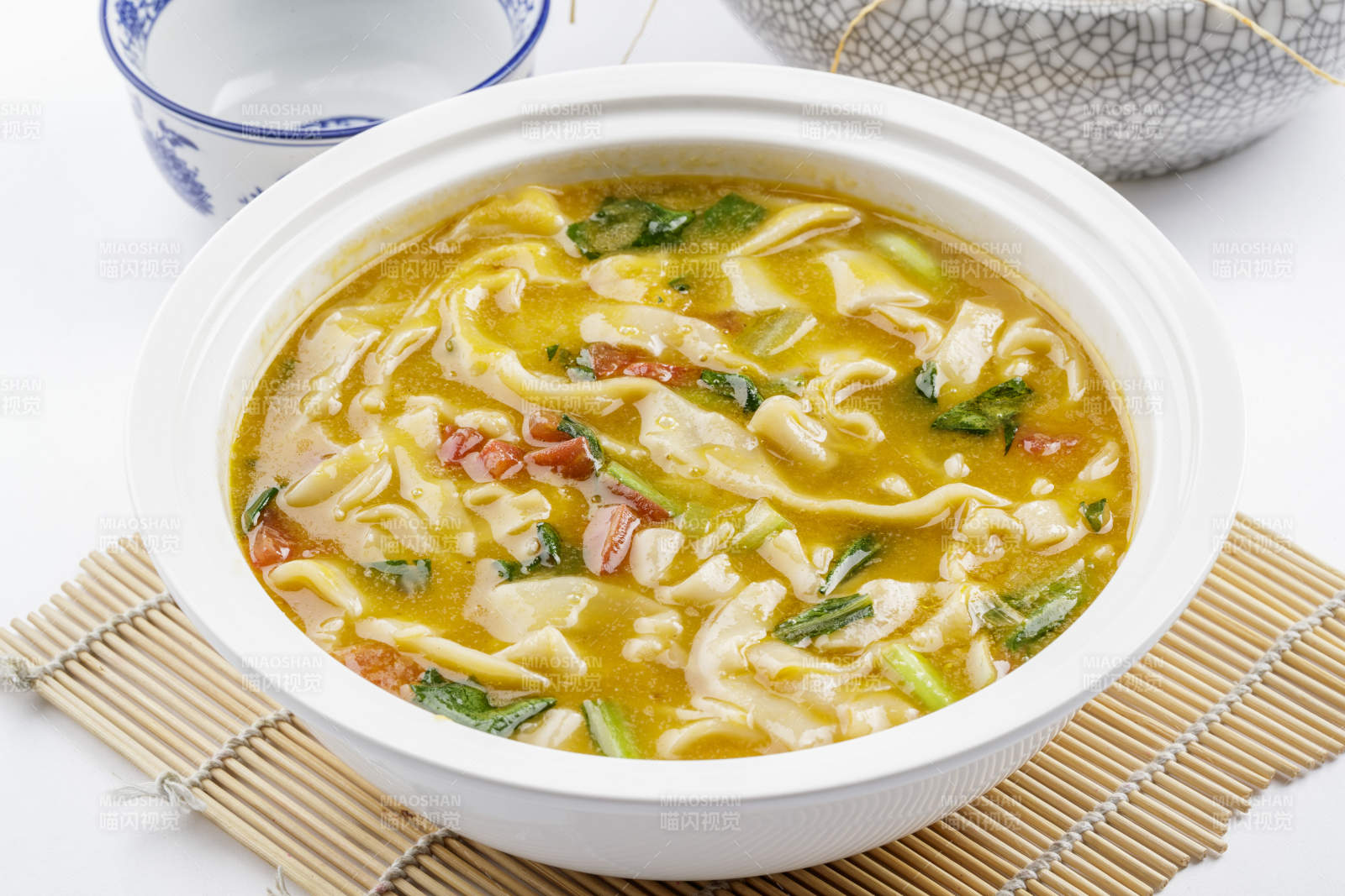 白色汤盆装的宽条打卤面摆放在寿司帘上图片