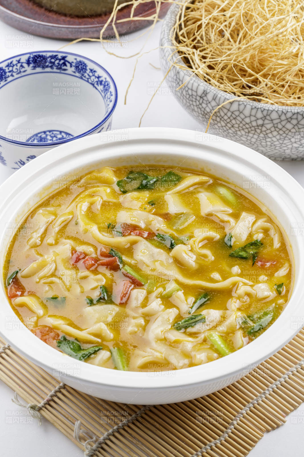 白色汤盆装的宽条打卤面摆放在寿司帘上图片