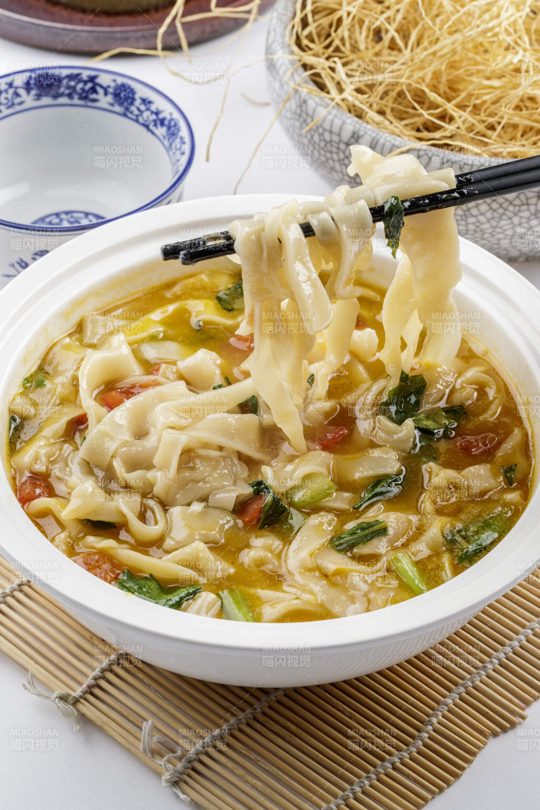 白色汤盆装的宽条打卤面摆放在寿司帘上图片