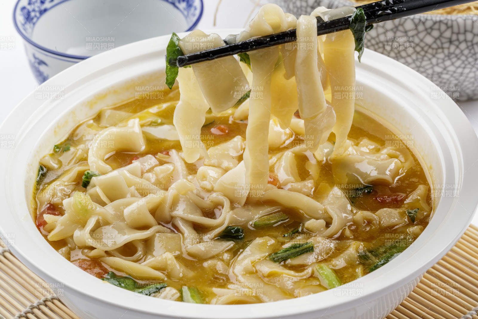 白色汤盆装的宽条打卤面摆放在寿司帘上图片