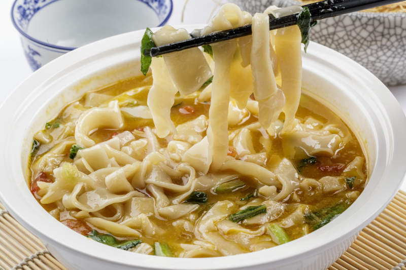 白色汤盆装的宽条打卤面摆放在寿司帘上图片