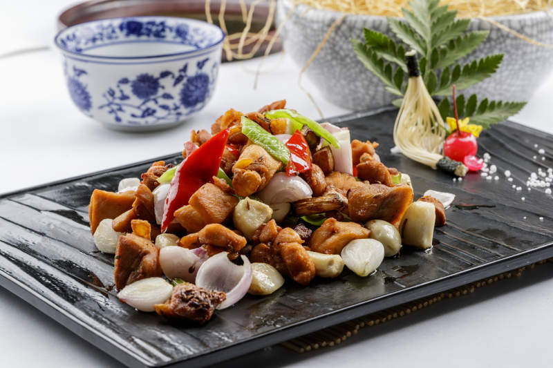 黑色石盘装的毛蒜烧猪腩肉摆放在白色背景上图片