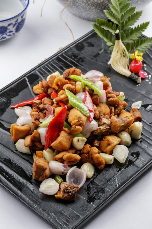 黑色石盘装的毛蒜烧猪腩肉摆放在白色背景上图片