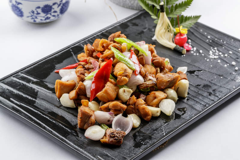 黑色石盘装的毛蒜烧猪腩肉摆放在白色背景上图片