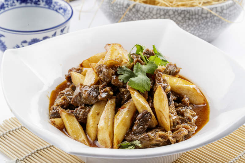 方形瓷盘装的长山药炖牛腩摆放在寿司帘上图片