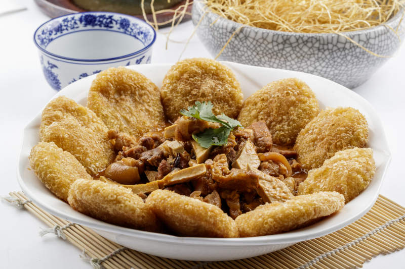 白色圆盘装的红扒肘子扒糕摆放在寿司帘上图片