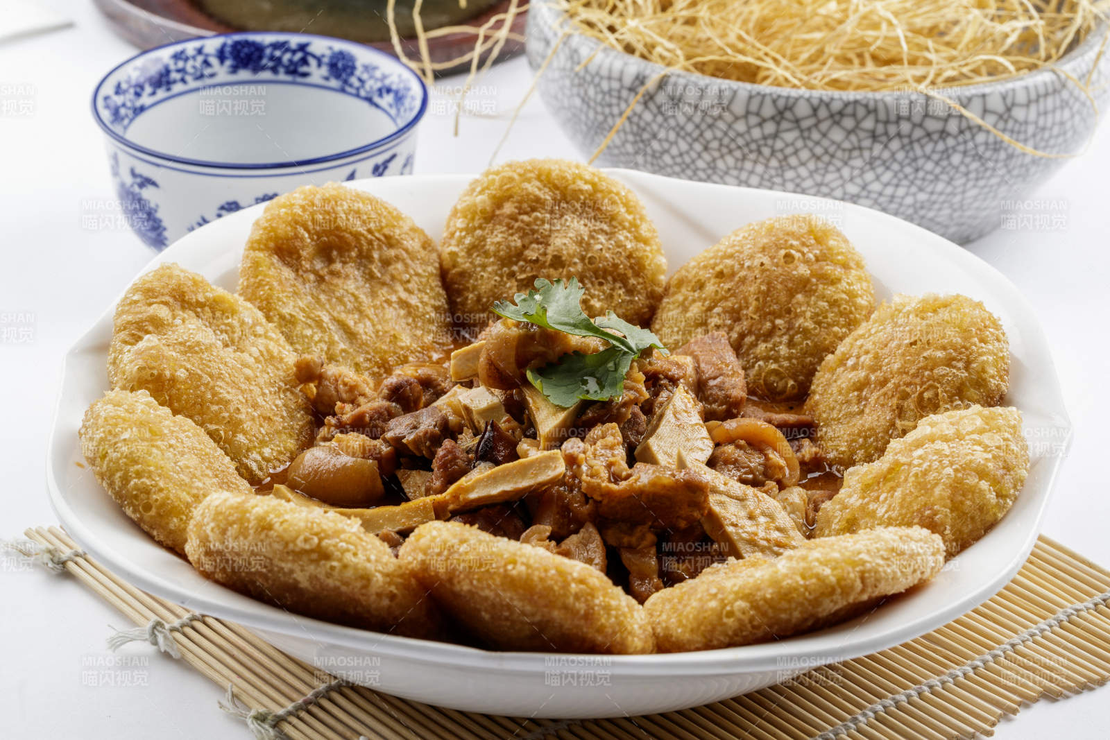 白色圆盘装的红扒肘子扒糕摆放在寿司帘上图片