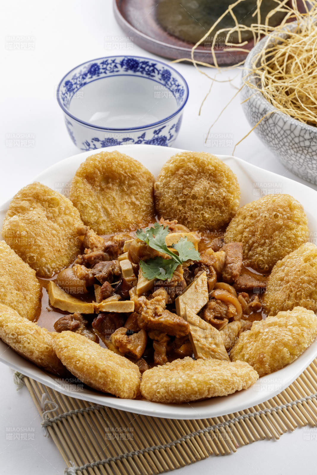 白色圆盘装的红扒肘子扒糕摆放在寿司帘上图片