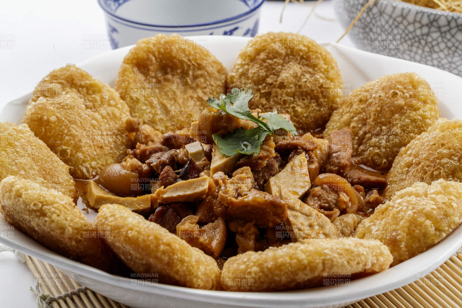 白色圆盘装的红扒肘子扒糕摆放在寿司帘上图片