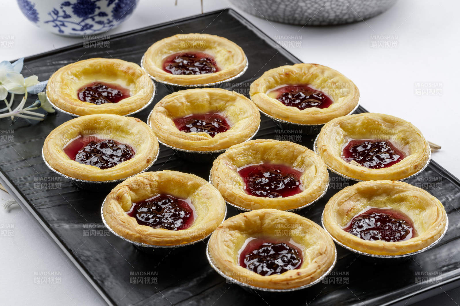 黑色盘子装的蓝莓蛋挞摆放在白色背景上图片
