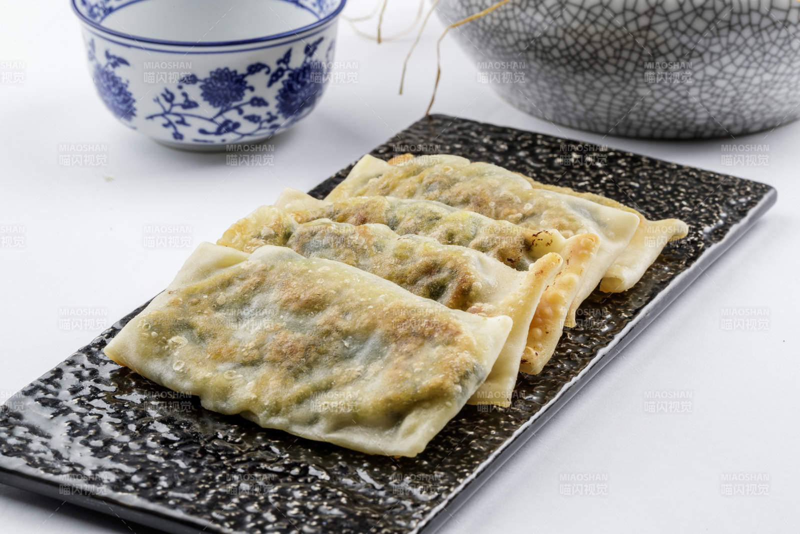 黑色磁盘装的香酥韭菜盒子摆放在白色背景上图片