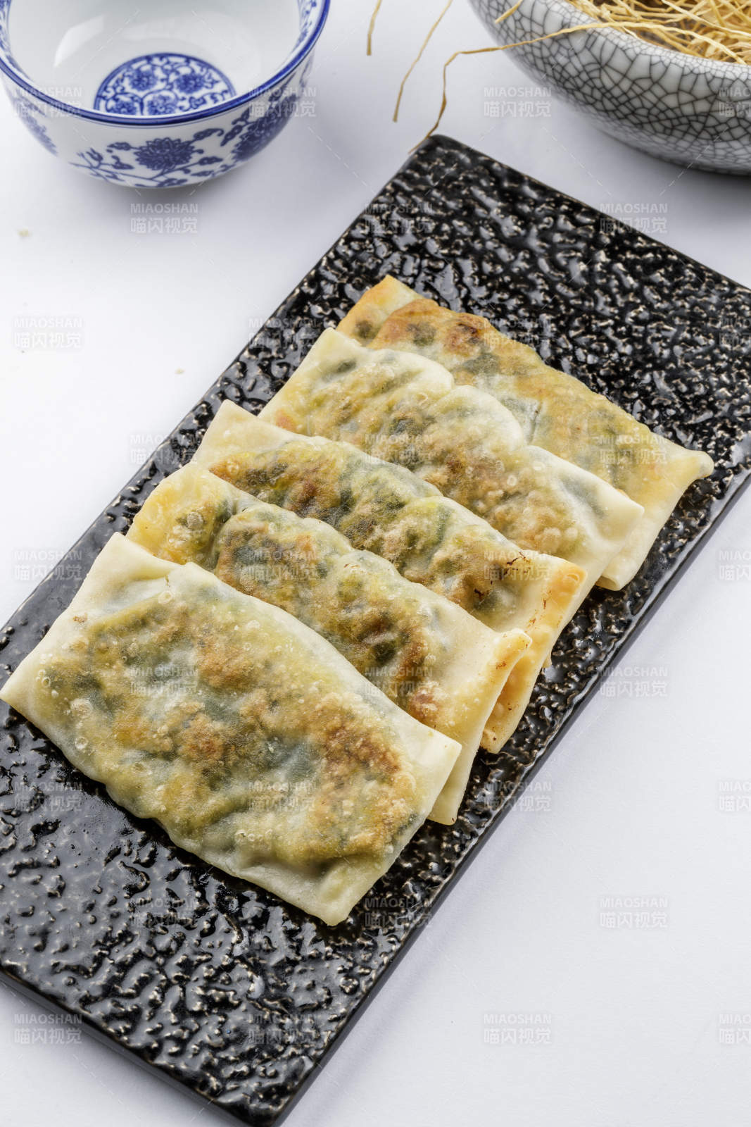 黑色磁盘装的香酥韭菜盒子摆放在白色背景上图片