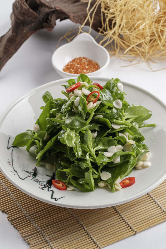 寿司帘上的圆瓷盘装的凉拌杏仁穿心莲图片