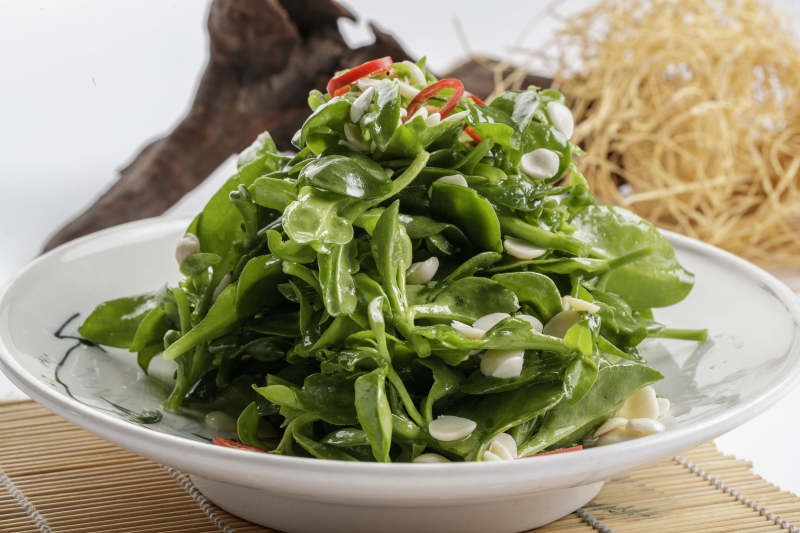 寿司帘上的圆瓷盘装的凉拌杏仁穿心莲图片