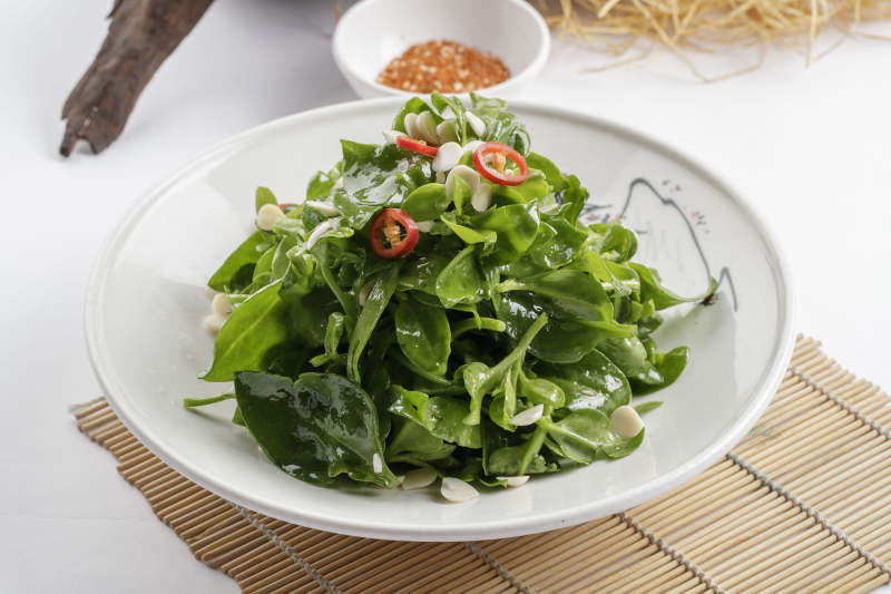 寿司帘上的圆瓷盘装的凉拌杏仁穿心莲图片