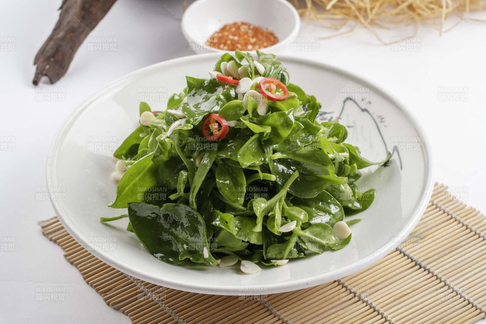 寿司帘上的圆瓷盘装的凉拌杏仁穿心莲图片