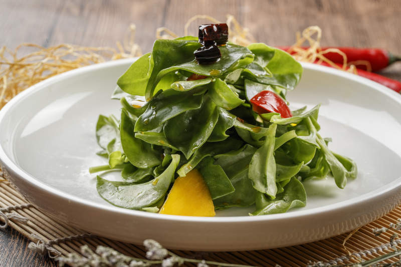 寿司帘上的圆瓷盘装的凉拌穿心莲图片