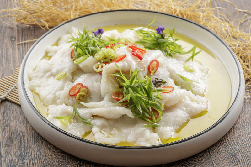 木质底纹上的圆瓷盘装的酸汤龙利鱼片图片