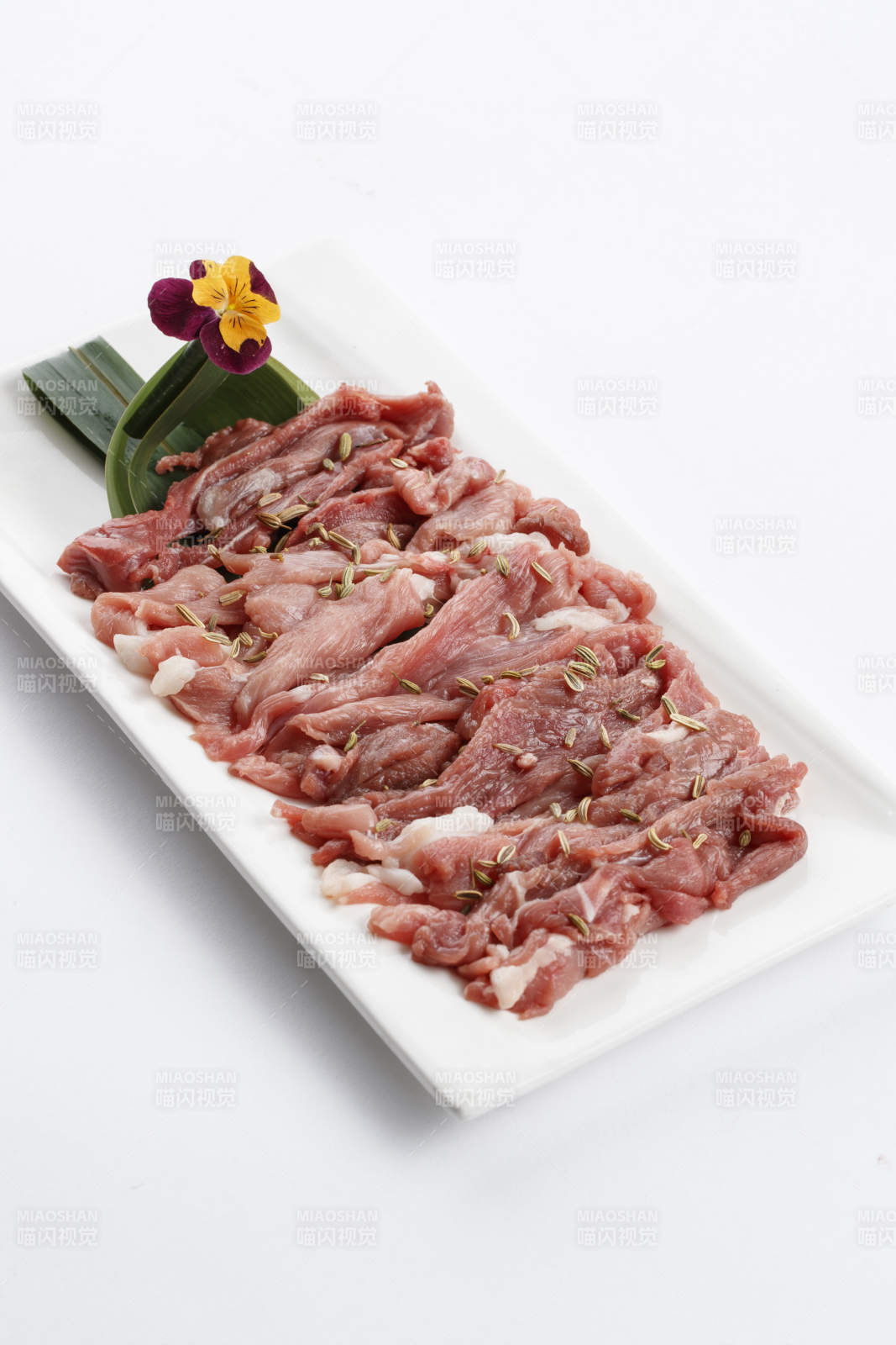 长方形白瓷盘装的鲜切羊后腿肉图片