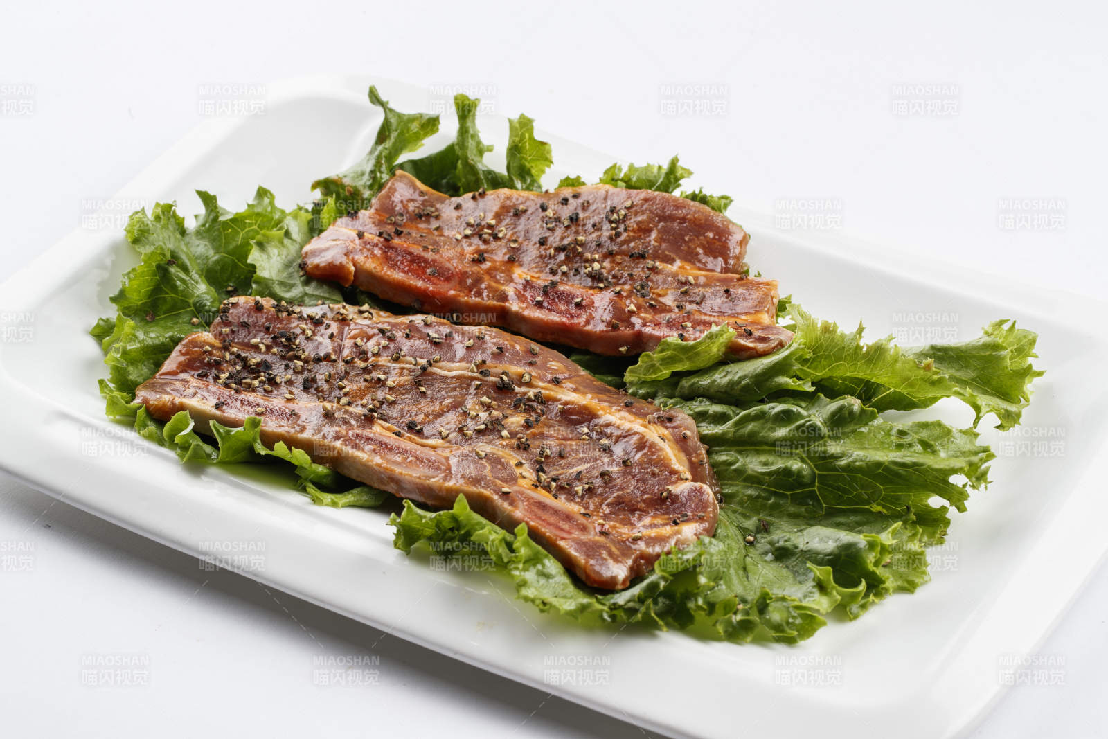 长方形白瓷盘装的黑胡椒腌制牛排肉图片