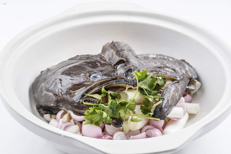 陈旧木板上的黑色砂锅装的浓汤生噘鲽鱼图片