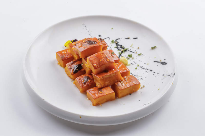 青瓷盘装的蜂蜜焗南瓜摆放在白色背景上图片