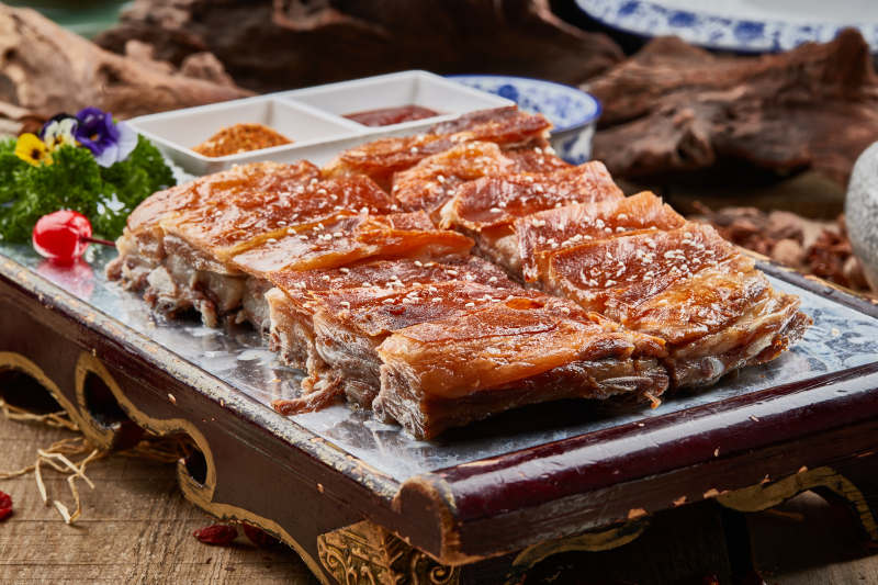 红色漆盘装的蒙古烤羊排摆放在樟木砧板上图片