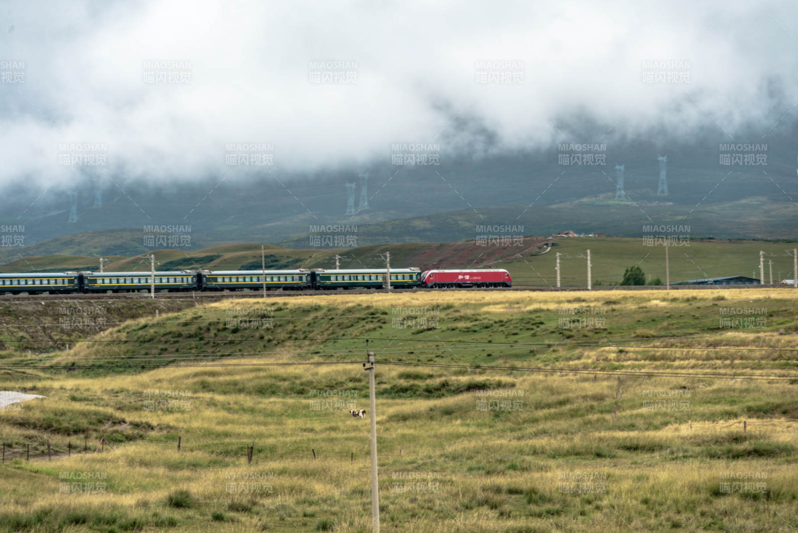 草原铁路上红色列车穿过云雾驶过高原山峦间图片