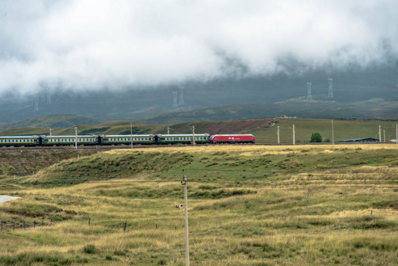 草原铁路上红色列车穿过云雾驶过高原山峦间图片