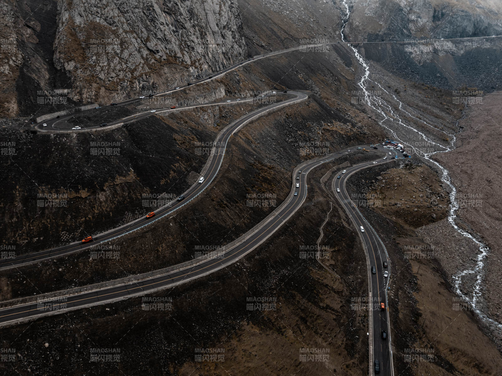 俯拍蜿蜒公路穿行岩壁河床的荒凉山地景致图片