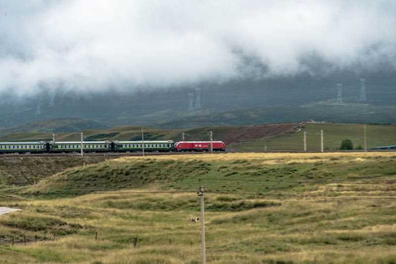高山草原上和谐号机车牵引绿皮火车穿云行驶图片