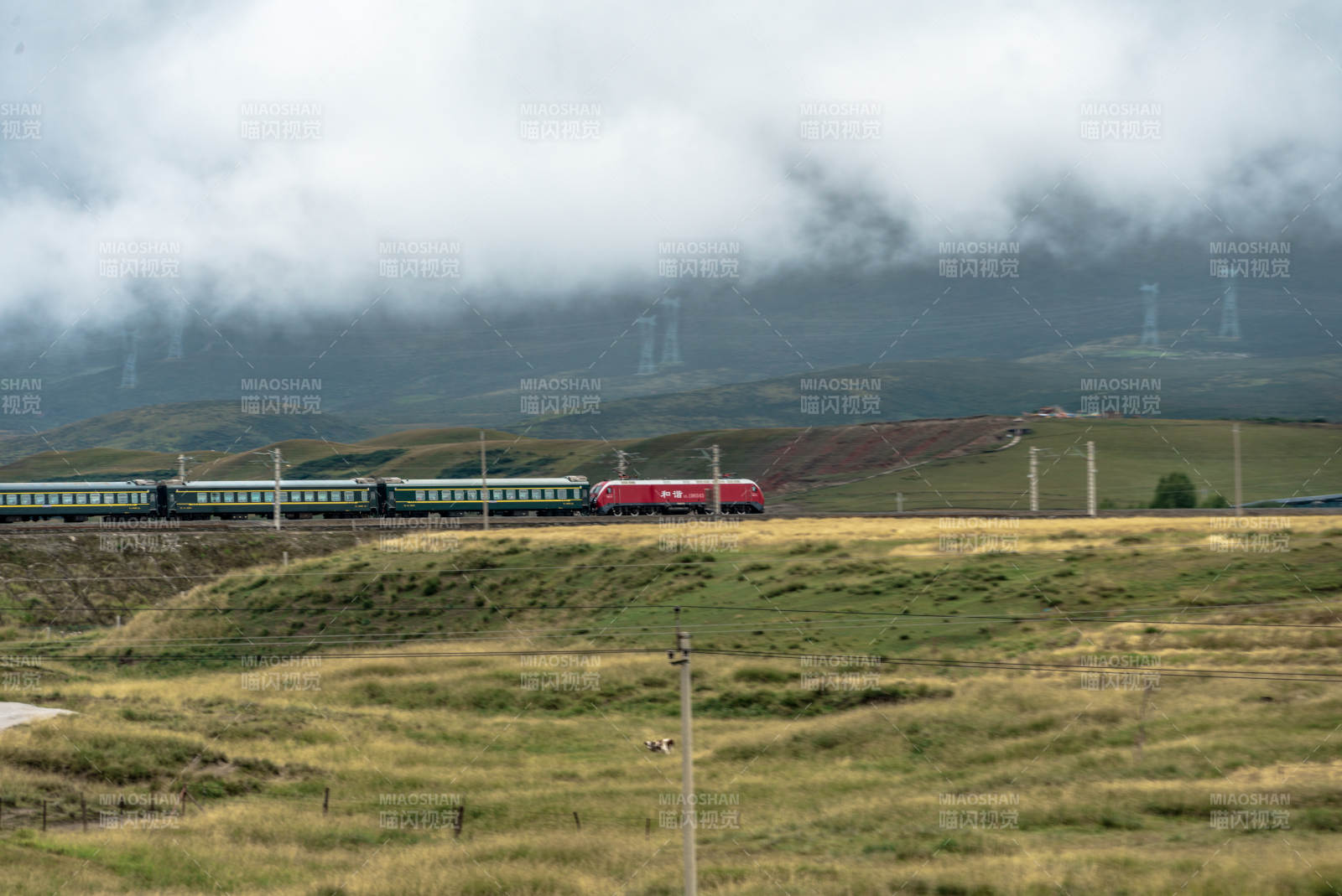 高山草原上和谐号机车牵引绿皮火车穿云行驶图片