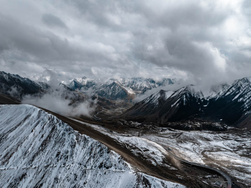雪山云雾缭绕下蜿蜒道路点缀的高山壮丽景观图片